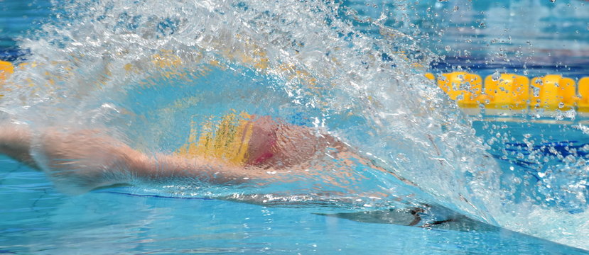 Man compete in swimming pool. Man swimming backstroke. Swimmer in swimming pool behind the water splash curtain.