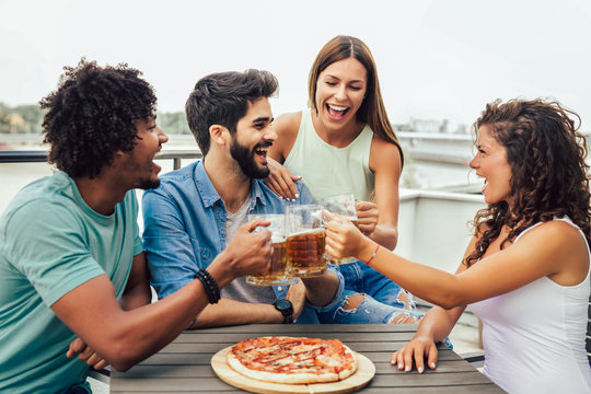 Friends enjoying pizza. Group of young cheerful people eating pizza and drinking beer while sitting at the bean bags on the roof of the building