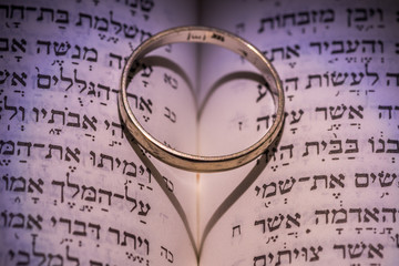 Close up of the Hebrew Jewish bible with a weeding ring creating a heart shape shadow 
