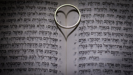 Fototapeta premium Close up of the Hebrew Jewish bible with a weeding ring creating a heart shape shadow 