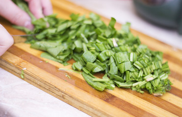 Woman cutting sorrel by knife on the wooden cooking desk
