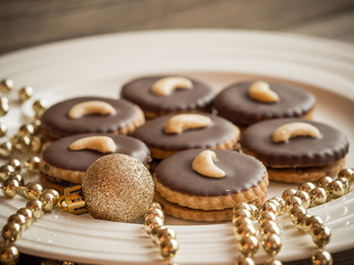 Naklejka premium Homemade Christmas sweets with cashew and dark chocolate, gold ornament and golden chain on a white plate