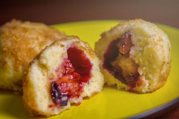 Fresh plum dumplings. One sliced dumpling and one hole on yellow plate on dark red table