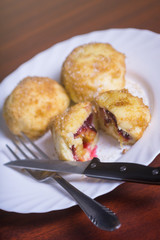 Fresh plum dumplings. One sliced dumpling and two whole with knife and fork on white plate on dark red table