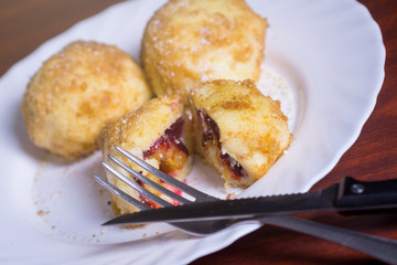 Fresh plum dumplings. One sliced dumpling and two whole with knife and fork on white plate on dark red table