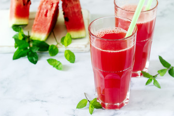 Cold watermelon lemonade with mint in a glass cup and slices of watermelon on a light background.