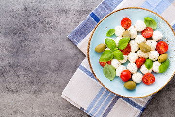 Delicious caprese salad with ripe cherry tomatoes and mini mozzarella cheese balls with fresh basil leaves.