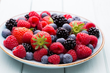 Fresh berry salad on blue dishes. Vintage wooden background.