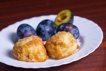 Fresh plum dumplings. Two dumplings with fresh plums on white plate on dark red table