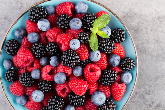 Fresh berry salad on blue dishes. Vintage wooden background.