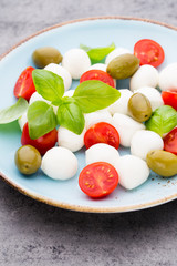 Fototapeta na wymiar Delicious caprese salad with ripe cherry tomatoes and mini mozzarella cheese balls with fresh basil leaves.