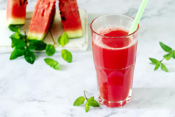 Cold watermelon lemonade with mint in a glass cup and slices of watermelon on a light background.