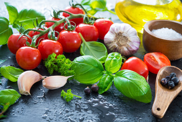 Ripe tomatoes with fresh basil, garlic and other herbs with water drops on slate plate