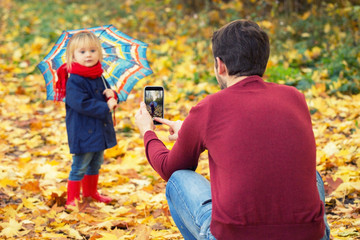 Father is making a selfie of his daughter in an autumn park.