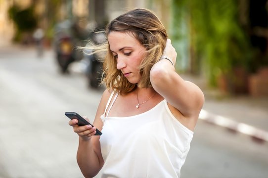 Beautiful young Caucasian fixing her hair and looking at her cellular phone. Phone addiction stock image. Convenient online shopping concept. New phone model.