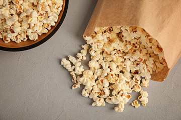 Paper bag and bowl with tasty popcorn on grey background, top view