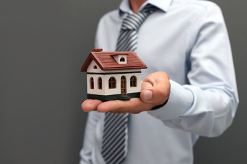 Real estate agent holding house model on gray background