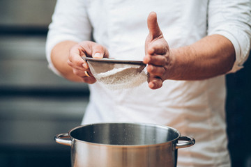 Men's hands chef sift the flour