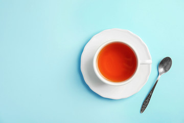 Cup of delicious tea with saucer and spoon on color background, top view