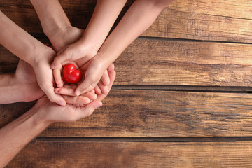 Family holding small red heart in hands on wooden background