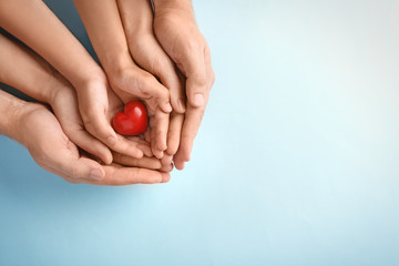 Family holding small red heart in hands on color background - obrazy, fototapety, plakaty
