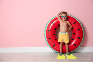 Fototapeta premium Cute little boy with inflatable ring wearing flippers near color wall