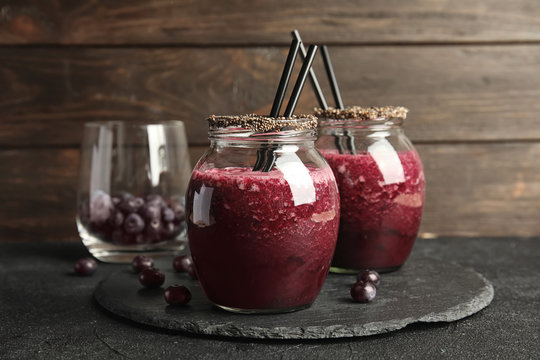 Jars of delicious acai juice with cocktail straws on dark table against wooden background