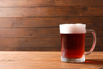 Glass mug with cold red beer on wooden table