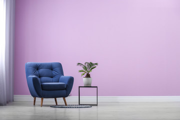 Stylish comfortable armchair near color wall