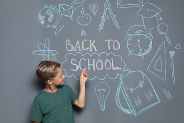 Little child near drawings and text BACK TO SCHOOL on grey background