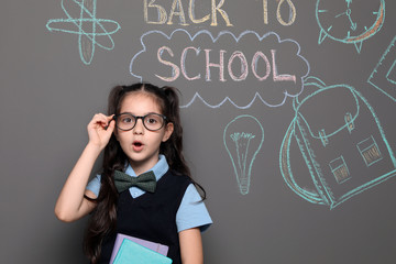 Little child in uniform near drawings with text BACK TO SCHOOL on grey background
