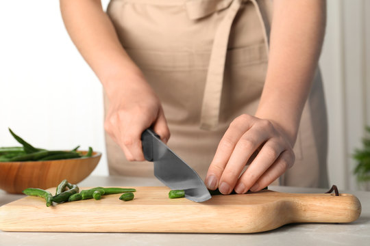 Woman cutting raw green beans for tasty dish at table