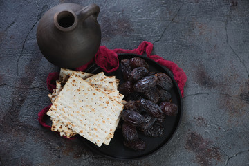 Metal tray with matzoh bread and dates and a clay jug over grey stone background, high angle view,...