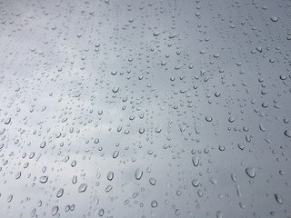 A view of the cloudy sky through the glass with drops from the rain. Background texture.