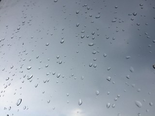 A view of the cloudy sky through the glass with drops from the rain. Background texture.