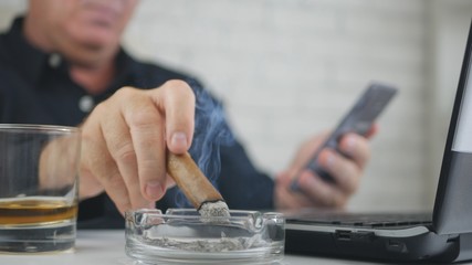 Fototapeta na wymiar Blurred Image with a Businessman Smoking Cigar Drinking Whisky Using Cellphone
