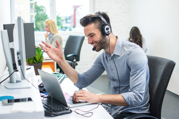 Portrait of handsome customer service executive with headset using laptop in office