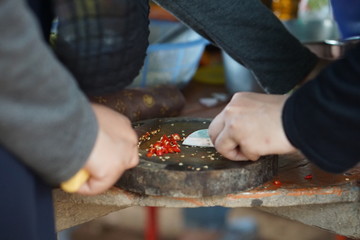 A group of young women cutting some red chilies on a small chopping board using a knife.