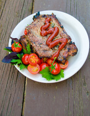 grilled steak meat with cherry tomatoes and greens on wooden old background