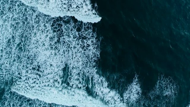 Strong waves on the evening beach with black sand in Indonesia, Bali. Aerial view. 4K