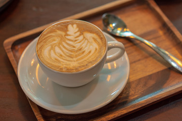 Latte art  coffee cup with saucer and spoon served on wooden tray