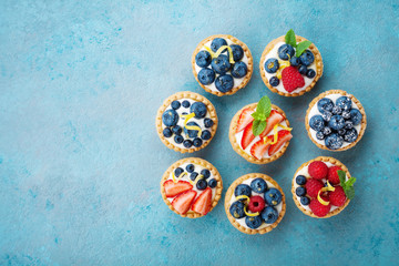 Tartlets or cake with cream cheese and berry on turquoise table from above. Delicious colorful...