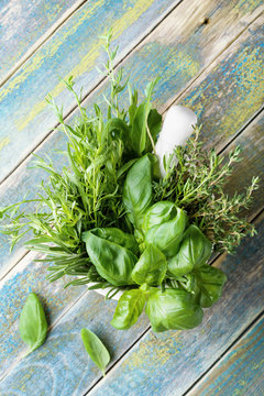 Aromatic herbs in mortar bowl on rustic wooden table top view. Basil, thyme, rosemary and tarragon. Fresh ingredients for cooking.