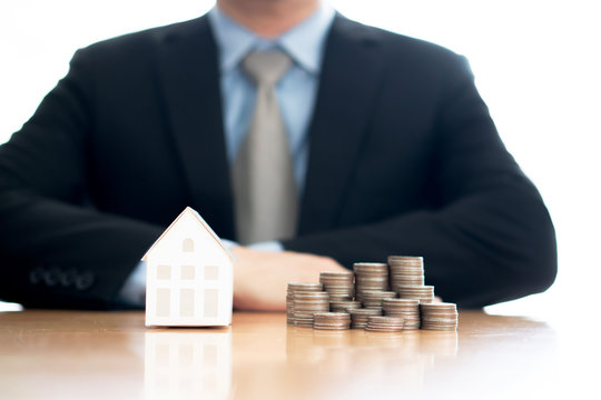 Stack of increasing coins and house model with businessman crossing his arms