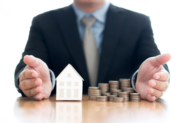 Stack of increasing coins and house model with businessman crossing his arms