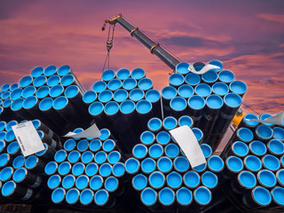 Big crane is stacking steel pipe in bundles at industrial port for exporting.
