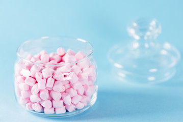 Fototapeta na wymiar Creative minimal still life on pastel blue colored background. Glass bowl with cute pink marshmallows. Copyspace