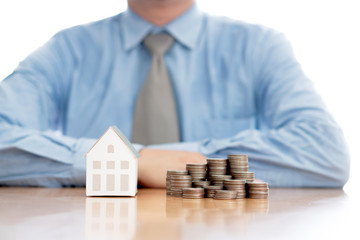 Stack of increasing coins and house model with businessman crossing his arms