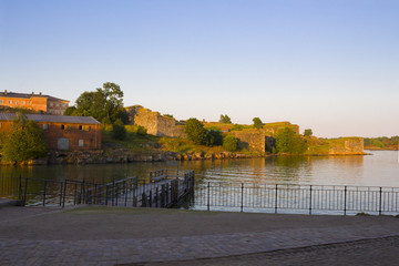 A wooden pier and old historical stone fortifications of Fort Suomnelinn in the Gulf of Finland near the city of Helsinki at the end of a summer day.