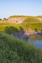 Obraz premium A small cove and old stone fortifications overgrown with grass in the old Fort Suomenlinna in the Gulf of Finland on a summer evening.